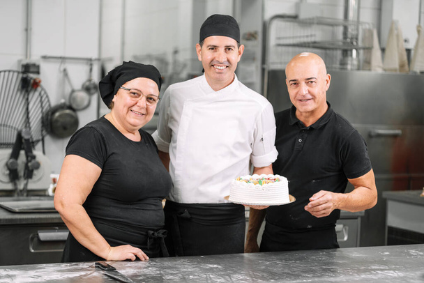 Equipo de chefs de pastelería sonriente mostrando un pastel. Grupo de trabajo de panadería. Equipo de chef
. - Foto, imagen