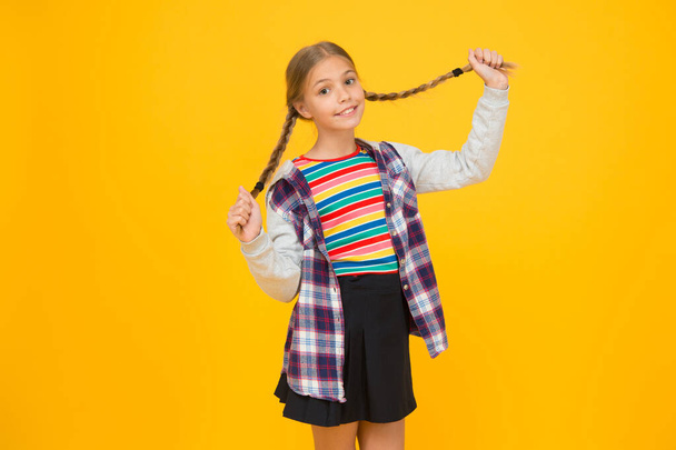 Long and braided. Adorable little child smile with long blond hair braids. Happy small girl hold long braided hairstyle yellow background. Long hair growth stimulant - Foto, Bild