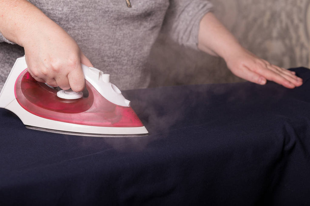 Ironing clothes. Female hands are ironing clothes with a red iron close-up.  - Photo, Image