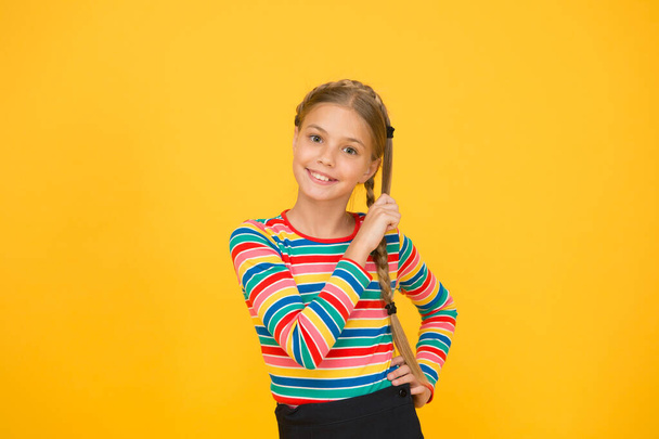 Braiding hair. Adorable little girl with plaited hair yellow background. Cute small child hold long hair braid. Luxurious hair extensions. Beauty salon. Haircare and hairstyling - Foto, imagen