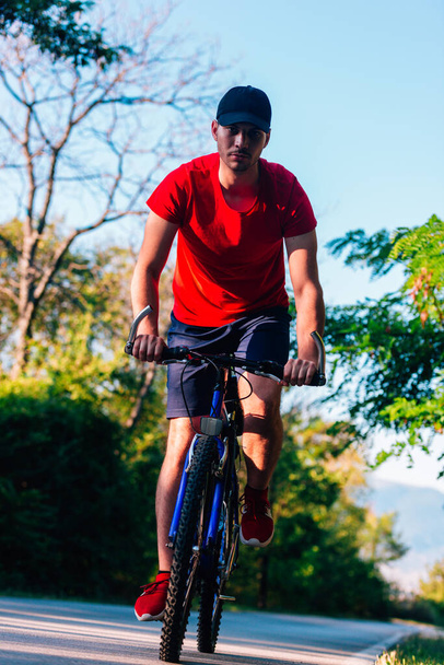 Fit ποδηλάτης βόλτες με το ποδήλατό του (ποδήλατο) σε ένα άδειο δρόμο στη φύση  - Φωτογραφία, εικόνα
