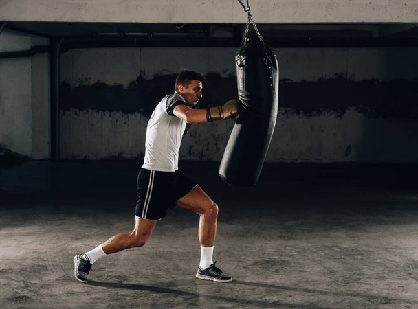 Joven luchador de kickboxing muscular practicando patadas con saco de boxeo
 - Foto, Imagen
