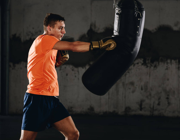 Mladý muž atlet boxerské cvičení ve fitness tělocvičně na tmavém pozadí.Atletický muž trénink hard.Kick box koncept - Fotografie, Obrázek