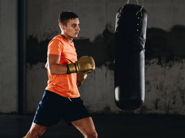 Spor salonunda boks eldiveniyle torba yumruklayan sportif bir erkek. Spor, spor, dövüş sanatları konsepti - Fotoğraf, Görsel