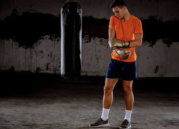 attraktiver junger Mann, der neben einem Boxsack trainiert und Boxhandschuhe trägt - Foto, Bild