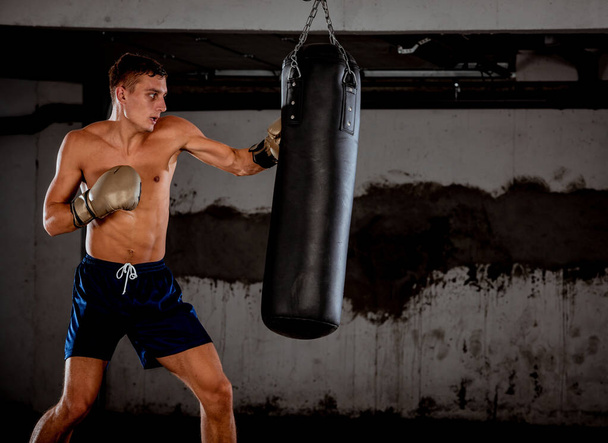 Silny kickboxer człowiek uderzając czarny piasek worek na tle siłowni - Zdjęcie, obraz