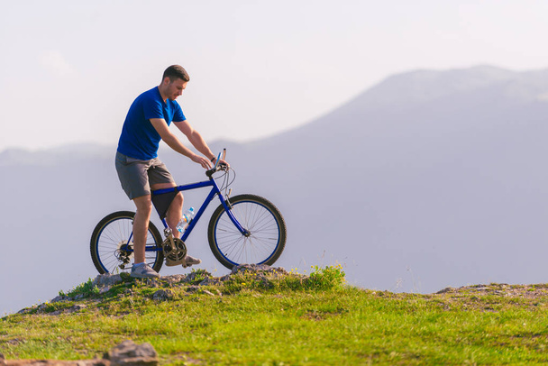 Fit Mountain Biker riding his bike through green grass on top of
 - Фото, изображение