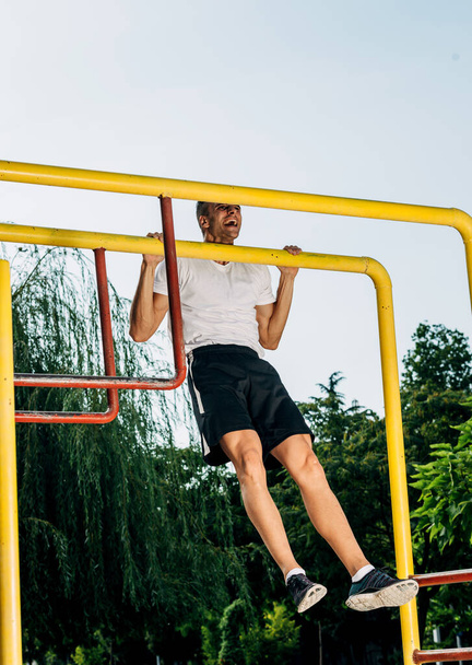 Man shakes his muscles on bar in city park. Crossfit concept - Photo, Image