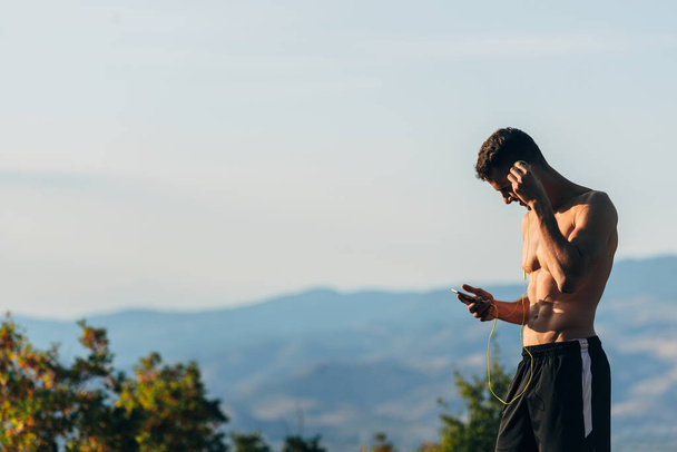 Sportovní chlap, který hledá hudbu na mobilu, zatímco se připravuje na běh - Fotografie, Obrázek