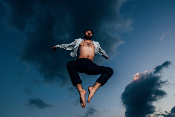 Σιλουέτα του νεαρού άνδρα πηδώντας κατά το βράδυ μπλε του ουρανού - Φωτογραφία, εικόνα