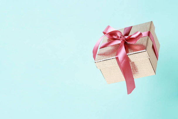 Boîte cadeau couleur or avec ruban rose sur fond bleu gros plan, espace de copie. Lévitation
 - Photo, image