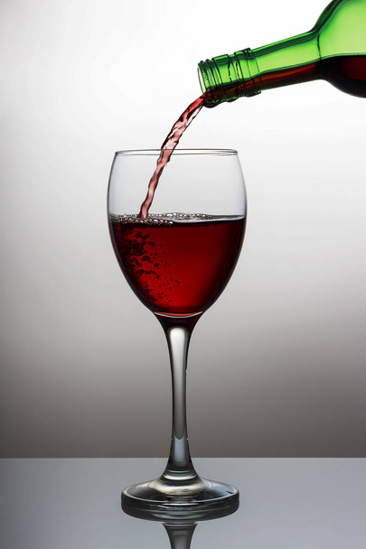 Einschenken von Rotwein in das Weinglas in Nahaufnahme, isoliert auf einem Hintergrund mit leichtem Gefälle - Foto, Bild