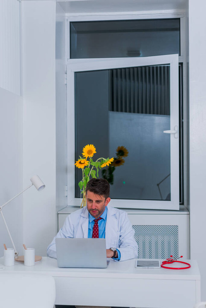 Άνδρας σοβαρός καυκάσιος γιατρός κάθεται στο γραφείο του μόνος και ου - Φωτογραφία, εικόνα