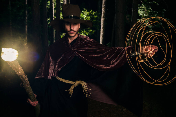 Mann in Zauberermantel und Mütze mit leuchtendem Stab - Foto, Bild