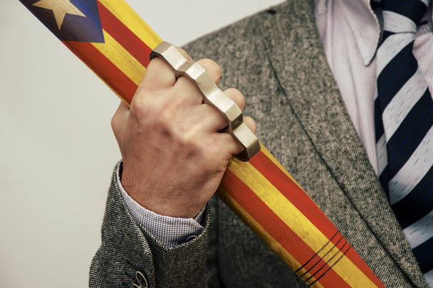 Um homem segura um morcego com a bandeira da Catalunha e dedos de bronze. Protestos de rua colidem com a polícia. Influência de danos corporais graves
. - Foto, Imagem