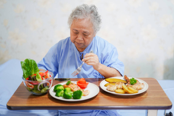 Aziatische senior of ouderen oude dame vrouw patiënt gezond eten van de ontbijt met hoop en gelukkig zittend en hongerig op bed in het ziekenhuis - Foto, afbeelding