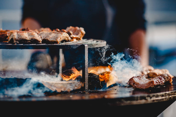 Vařit grily steaky a vepřové žebírka zahájit oheň. Obrátí maso s kleštěmi. Koncept pouličního jídla - Fotografie, Obrázek