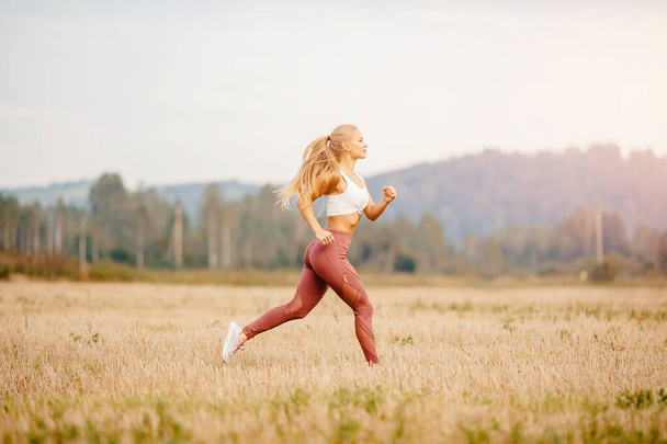 Αθλητική νεαρή ξανθιά κοπέλα είναι τζόκινγκ στο πάρκο αυγή, έννοια τρέχει για την υγεία - Φωτογραφία, εικόνα