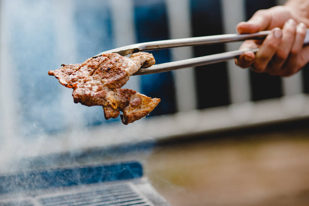 A grillezett steak és a sertésborda tüzet nyit. Megfordítja a húst fogóval. Utcai élelmiszer fogalma - Fotó, kép