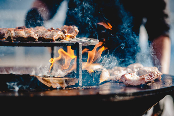 Cocine a la parrilla filetes y costillas de cerdo abrir fuego. Da vuelta la carne con pinzas. Concepto de comida callejera
 - Foto, imagen