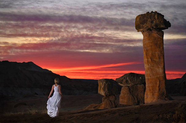 Mujer rubia en vestido blanco por los taburetes gigantes de roca viendo la puesta de sol en el desierto de roca en Arizona
.  - Foto, imagen
