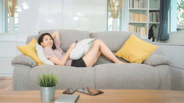 Молодая азиатская девушка-подросток смотрит телевизор дома, женщина чувствует себя счастливой, лежа на диване в гостиной. Стиль жизни женщина расслабиться утром на домашней концепции.  - Фото, изображение