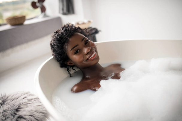 Cheerful woman feeling happy while relaxing in bath - Foto, afbeelding