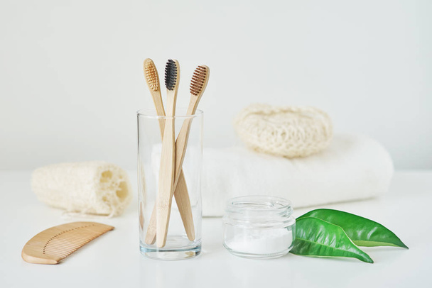 Καμία ιδέα για πλαστικά μηδενικά απόβλητα. Οικολογικά ξύλινες οδοντόβουρτσες μπαμπού σε ποτήρι, πετσέτα, οδοντωτή σκόνη και πετσέτα σε λευκό φόντο - Φωτογραφία, εικόνα