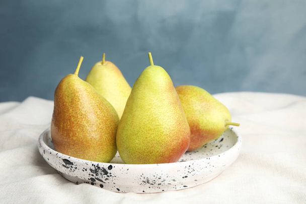 Plate with ripe juicy pears on light fabric against blue background - Foto, Bild