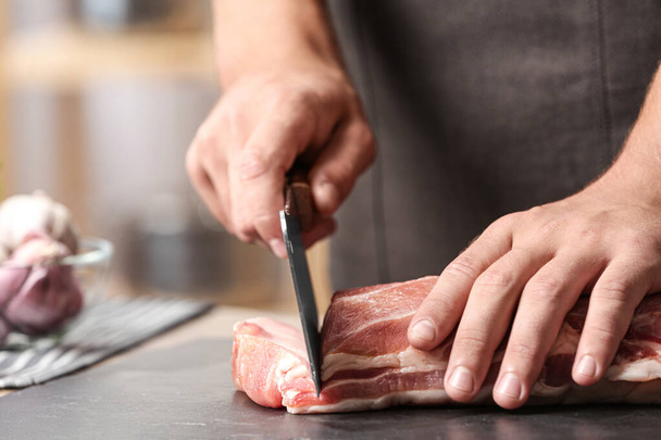 Man cutting fresh raw meat on table in kitchen, closeup - Фото, изображение