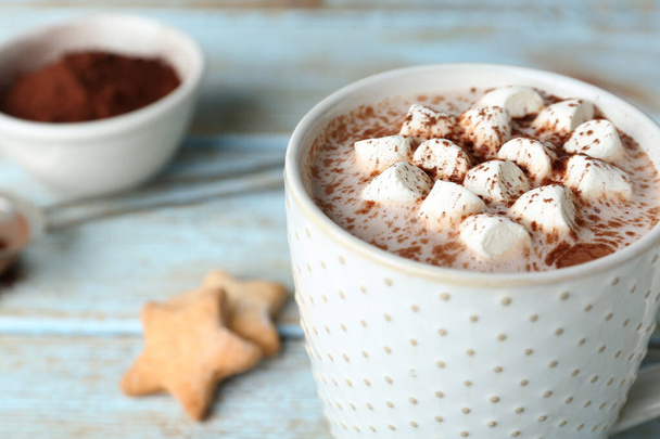 Delicious hot cocoa drink with marshmallows in cup on light blue wooden table, closeup - Valokuva, kuva