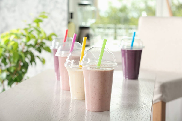 Different milk shakes in plastic cups on white wooden table indoors - Photo, Image