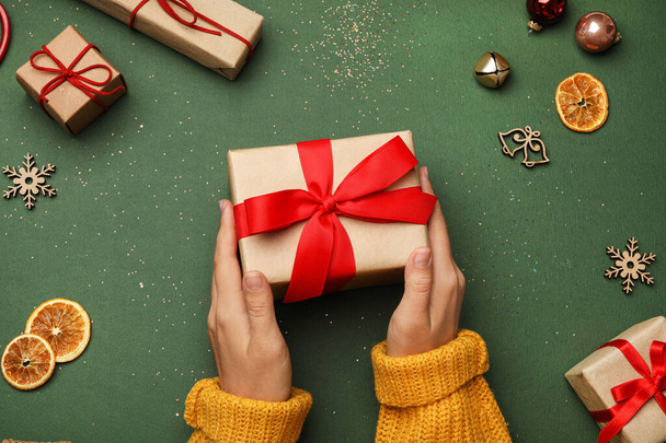 Young woman holding Christmas gift on green background, flat lay - Fotografie, Obrázek