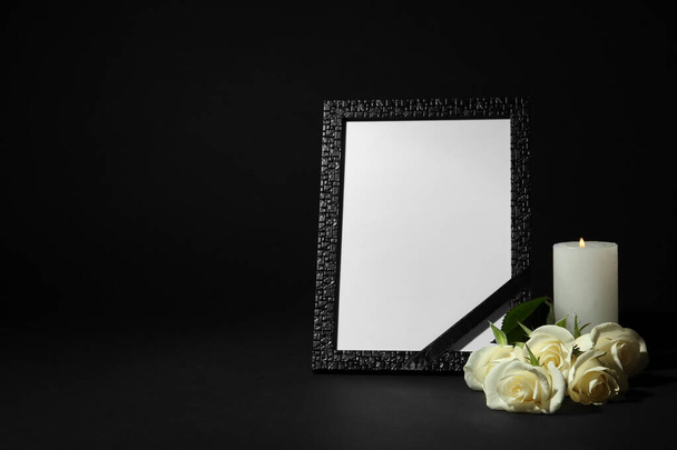 Funeral photo frame with ribbon, white roses and candle on dark table against black background. Space for design - Fotografie, Obrázek