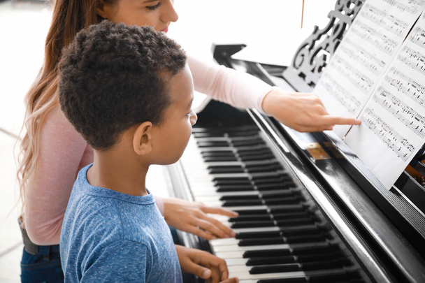 Mujer enseñando a un niño afroamericano a tocar el piano en casa
 - Foto, imagen