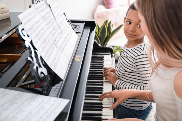 Woman teaching little African-American boy to play piano at home - Фото, изображение