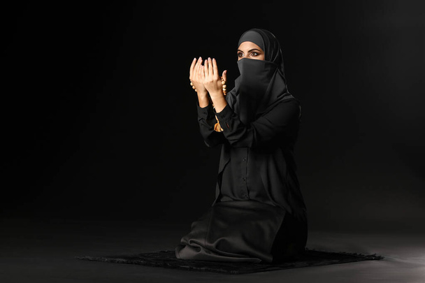 Kaunis musliminainen rukoilee tummaa taustaa vasten
 - Valokuva, kuva
