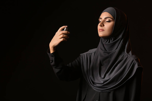 Beautiful Muslim woman with perfume on dark background - Photo, Image