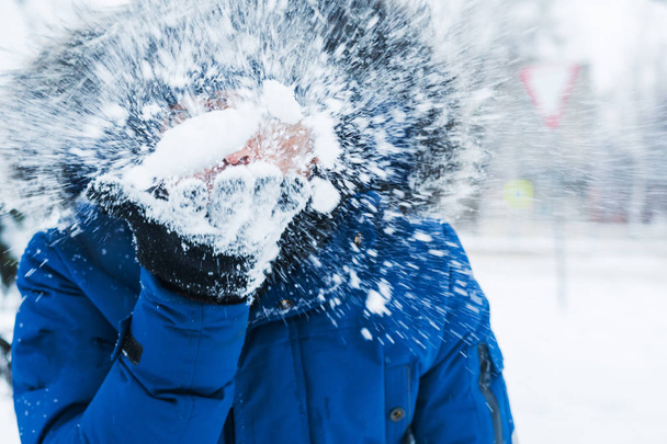 Mężczyzna trzymający śnieg w rękach i dmuchający na niego - Zdjęcie, obraz