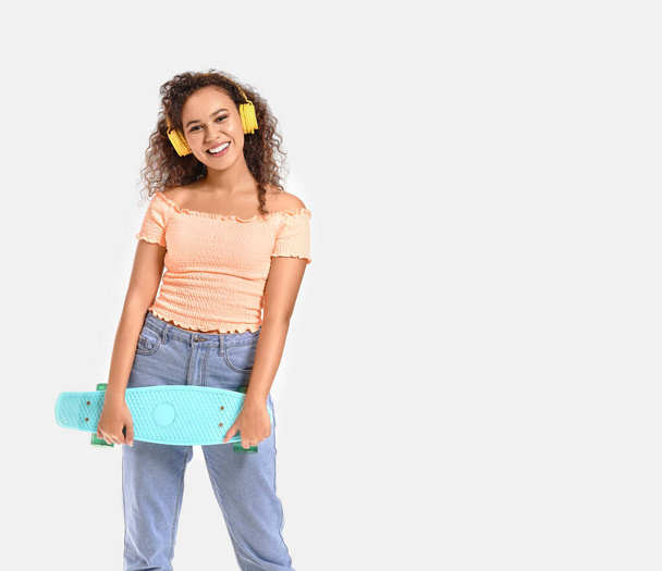 Beautiful African-American woman with skateboard listening to music on white background - Fotografie, Obrázek