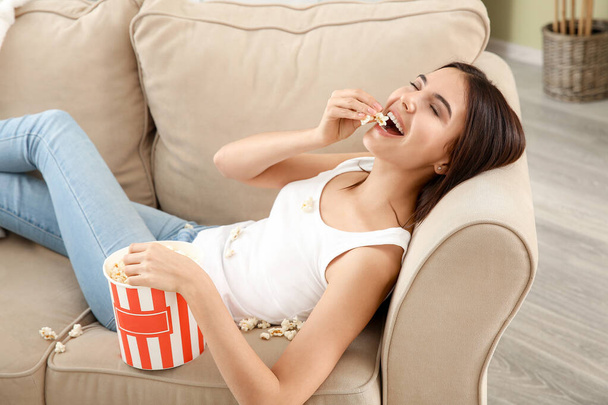Молодая женщина ест попкорн на диване дома
 - Фото, изображение