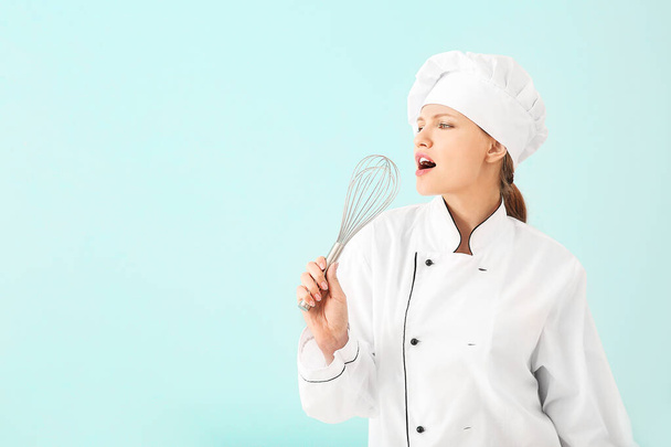 Beautiful female chef using whisk as microphone for singing on light background - Foto, imagen