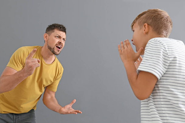 Arguing father and his little son on grey background - Foto, afbeelding