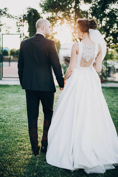 Gorgeous bride and groom walking in sunset light. Beautiful styl - 写真・画像