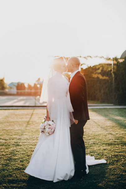 Stylish bride and groom gently kissing in sunset light. Beautifu - Foto, afbeelding