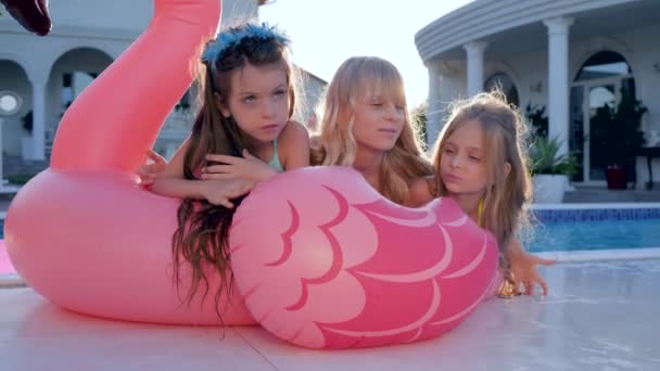 Маленькие девочки лежат на надувных розовых фламинго возле бассейна, дети знаменитости в купальниках на летних каникулах, избалованные богатые дети
 - Кадры, видео