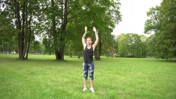 sprawna i wysportowana kobieta ćwicząca w zielonym parku przed joggingiem - Materiał filmowy, wideo