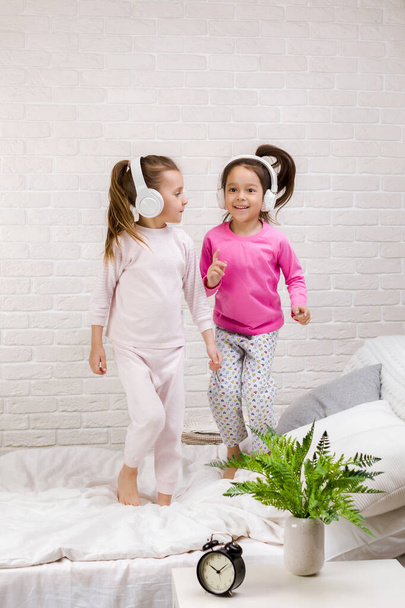 little children girls listening to the music with the headphones and dancing on bed. - Foto, imagen
