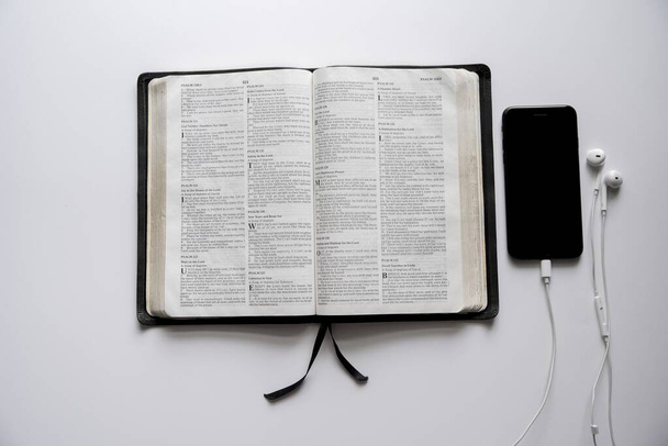Overhead tiro de uma bíblia aberta perto de um smartphone em uma superfície branca
 - Foto, Imagem