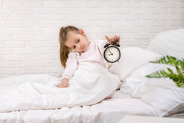 Little girl in pyjamas with clock - Fotoğraf, Görsel